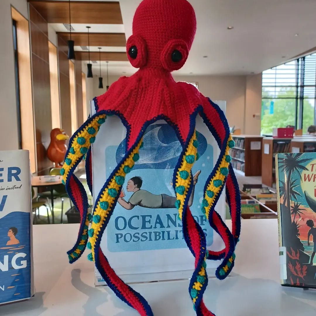 Crocheted Octopus sitting atop a library flyer sign