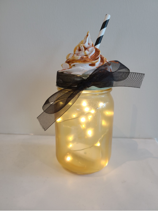 Glass jar with lights inside; top is decorated with fake whipped cream and a straw.