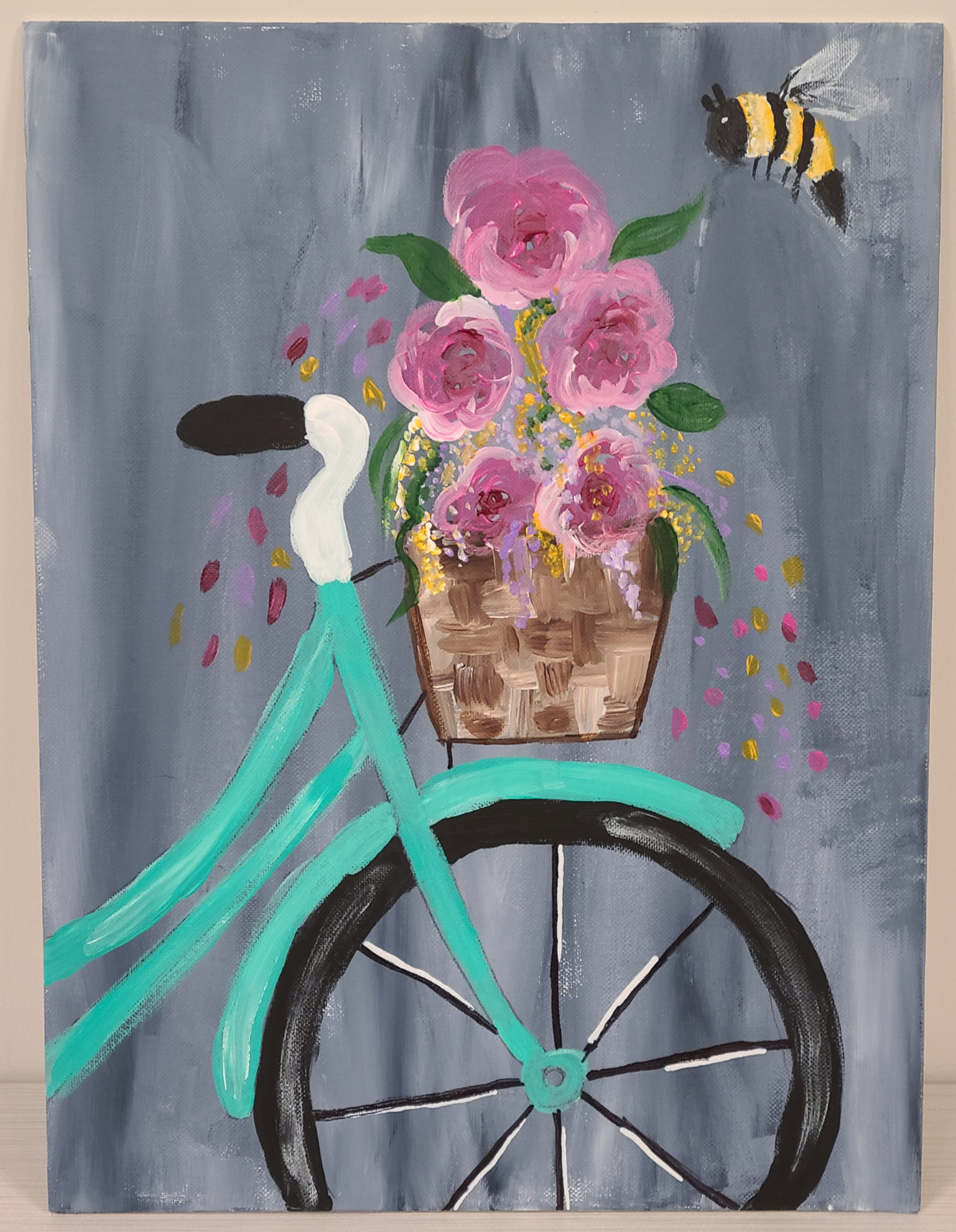 Teal bicycle with brown woven basket with pink flowers and a bumblebee