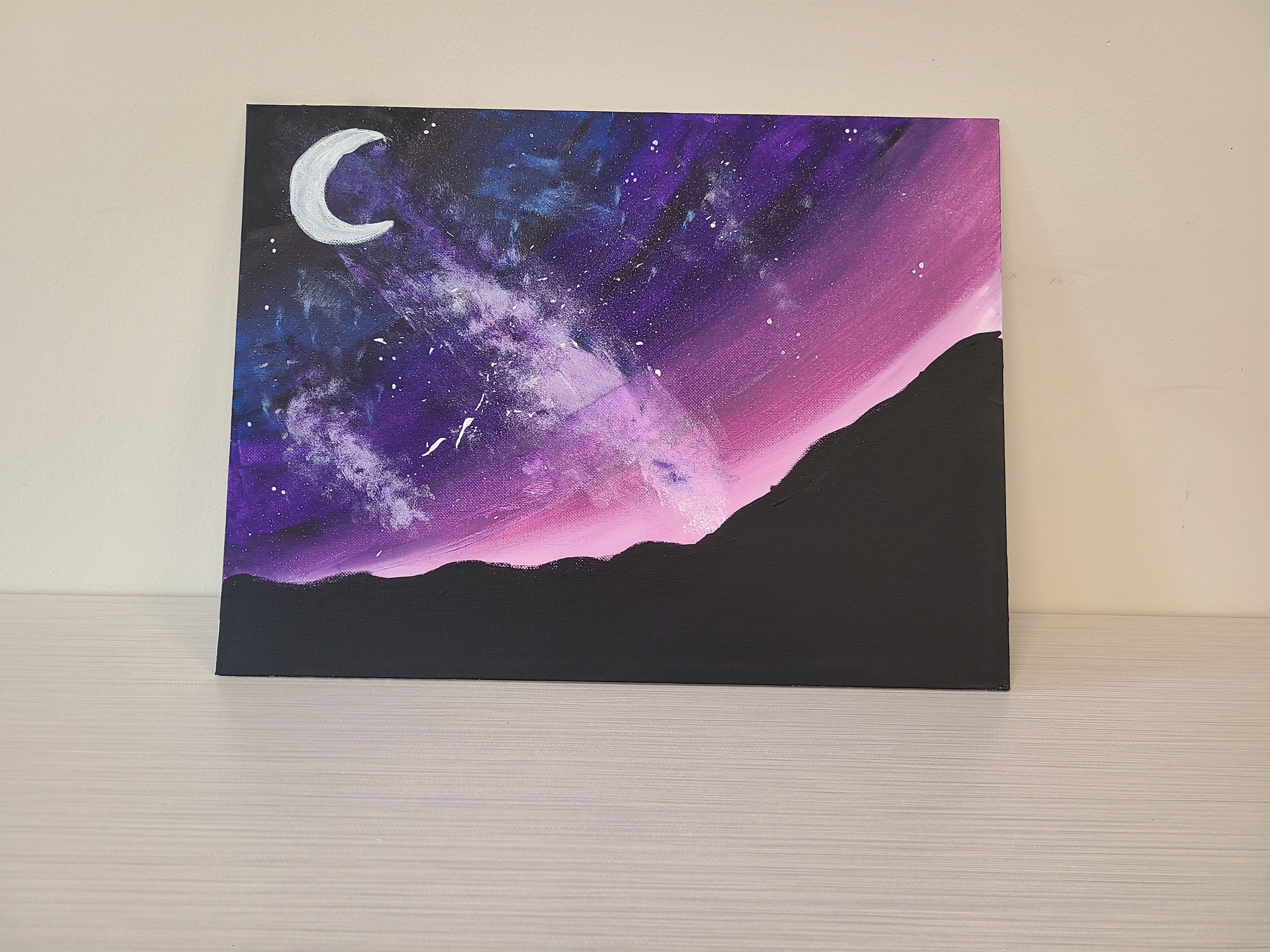 Night sky scene in black, blue, purple and pink with white crescent moon