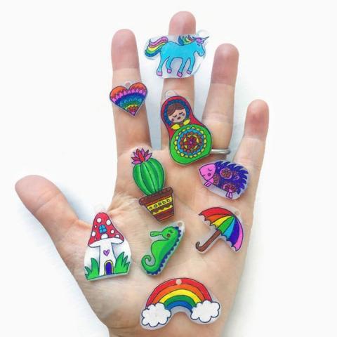 Nine completed shrinky dink crafts displayed on top of a human hand.