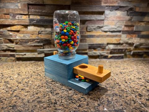 Wooden candy dispenser in blue with a glass jar filled with colorful candies