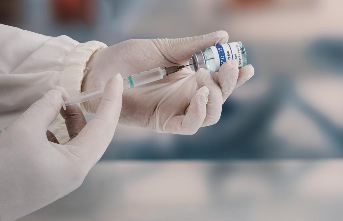 a pair of gloved hands holding a needle and a vial of vaccine