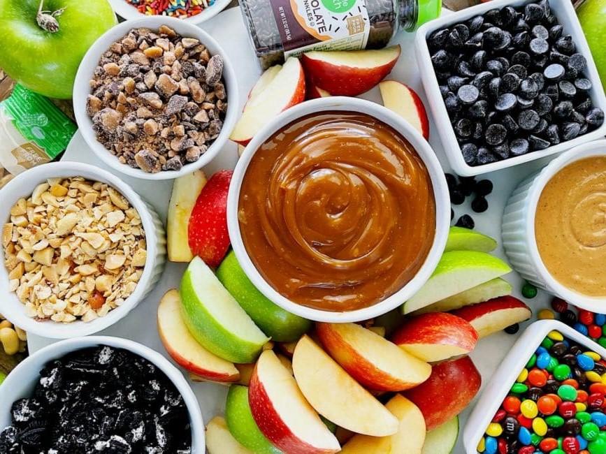 Apple slices surrounding a bowl of caramel and assorted toppings